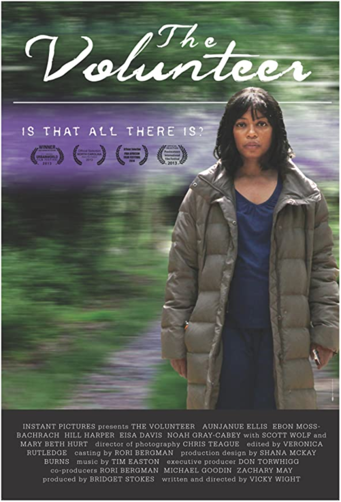 The film poster showing Leigh (Aunjanue Ellis) wearing a shapless gray coat in a blurry green landscape.