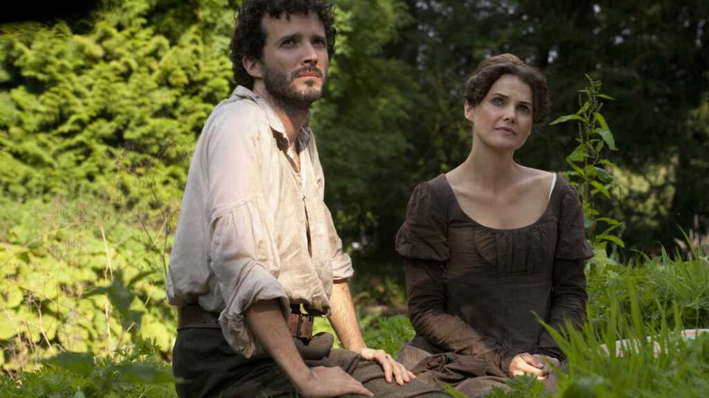 Jane (Keri Russell) and Martin (Bret McKenzie) sitting in the grass together. 