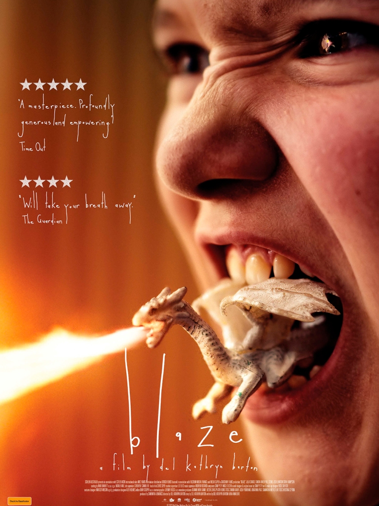 The film poster showing Blaze (Julia Savage) with a little white dragon figure in her mouth. The dragon is spitting fire.