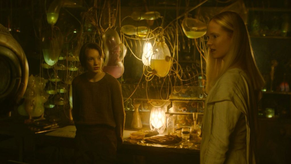 Vesper (Raffiella Chapman) standing in her lab together with Camellia (Rosy McEwen). 