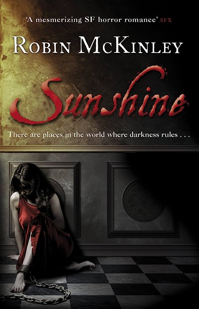 The book cover showing a chained up woman in a red dress sitting on the floor, barely touched by sunshine.